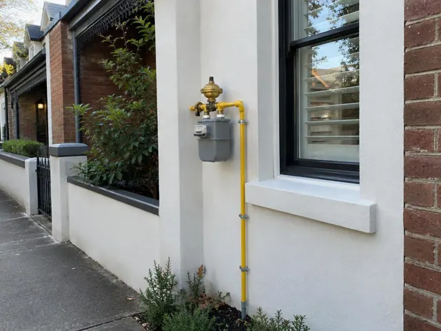 Exterior gas meter and yellow pipe on a rendered brick house wall beside a window in Paddington